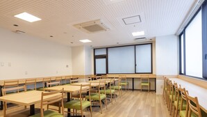 A conference room with multiple tables and chairs, a large projection screen, and a view of the outside through large windows. - Hotel Wingport (Nagasaki)