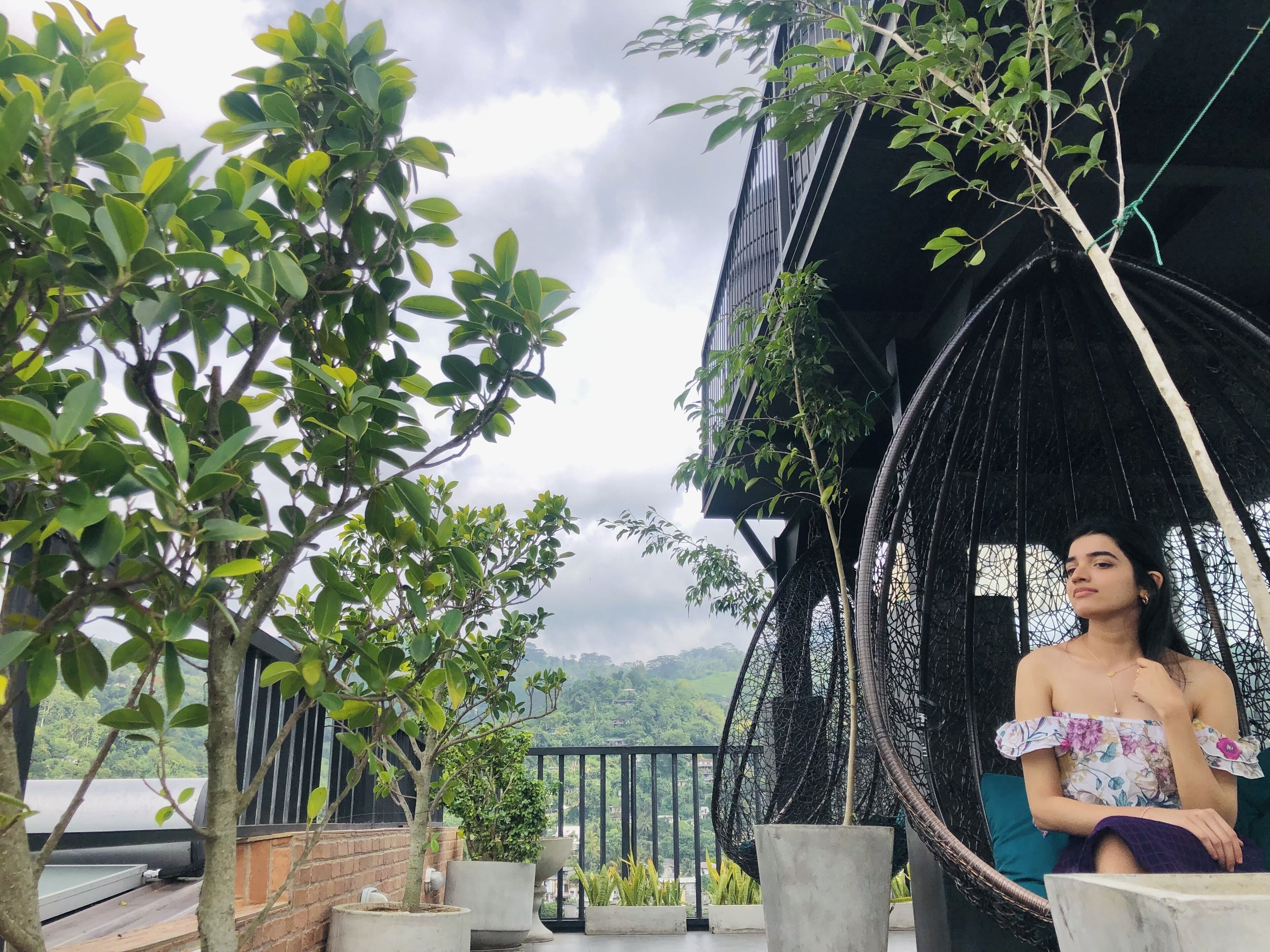 A balcony with potted plants, a hanging chair, and a view of a mountainous landscape.