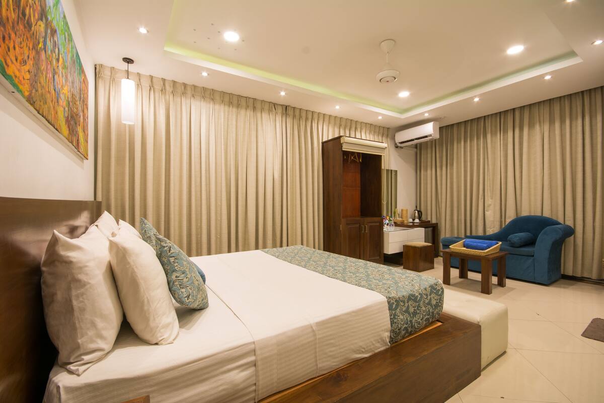 A hotel room with a bed, a desk, a chair, and an air conditioning unit.