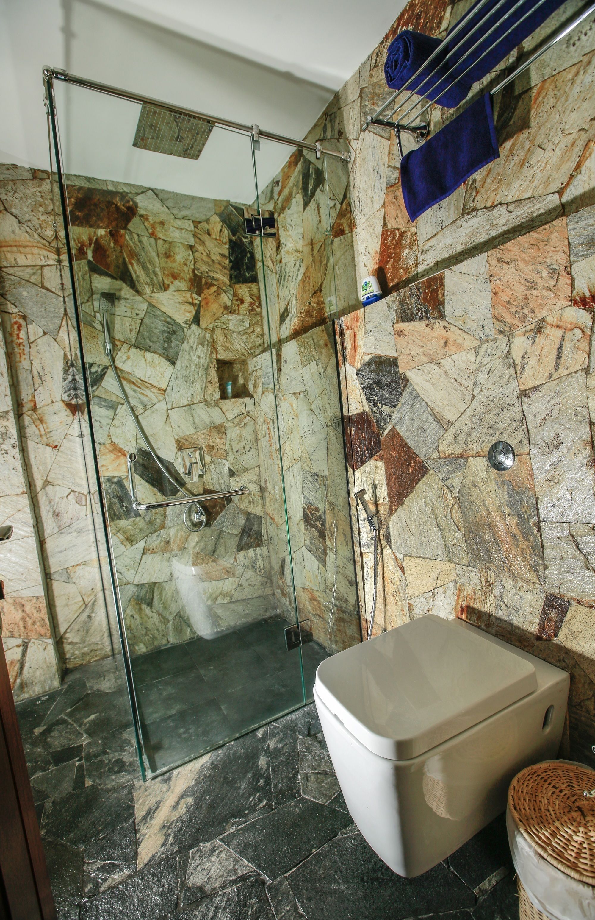 A bathroom with a glass-enclosed shower, a toilet, and a stone-patterned wall.