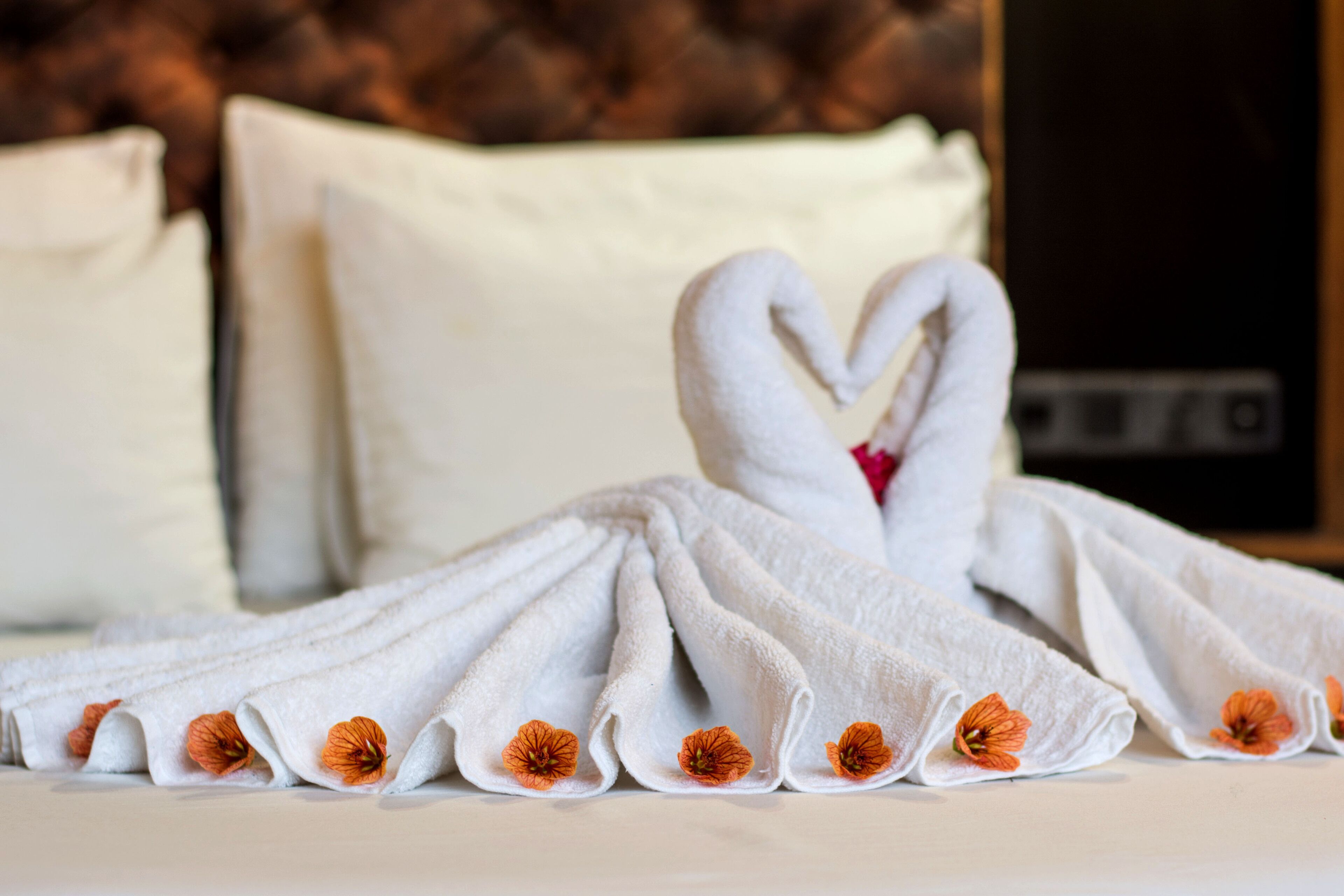 A neatly folded towel with a heart shape and orange flowers on a bed.