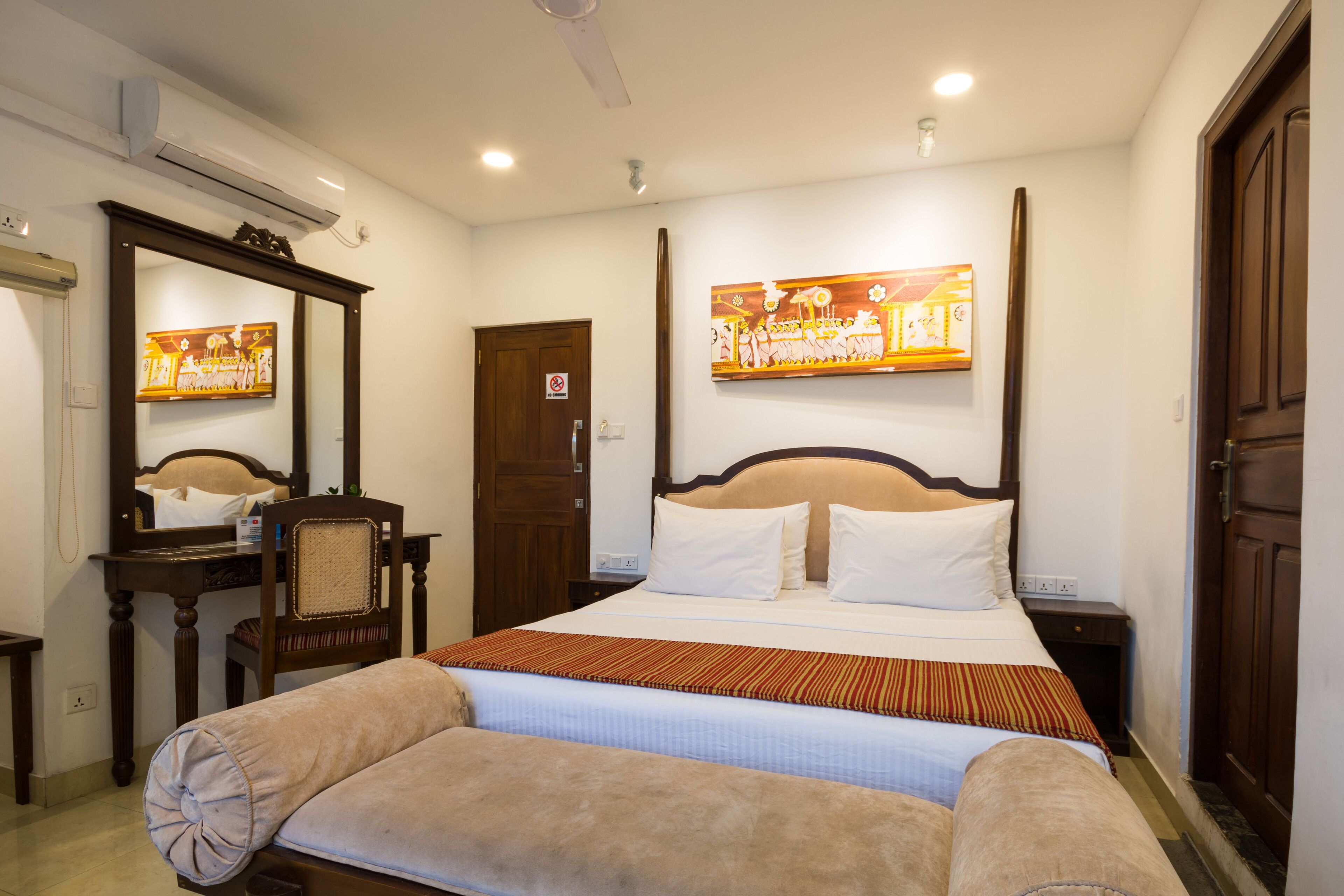 A neatly arranged hotel room with a large bed, a bedside table, a chair, a mirror, and a door.