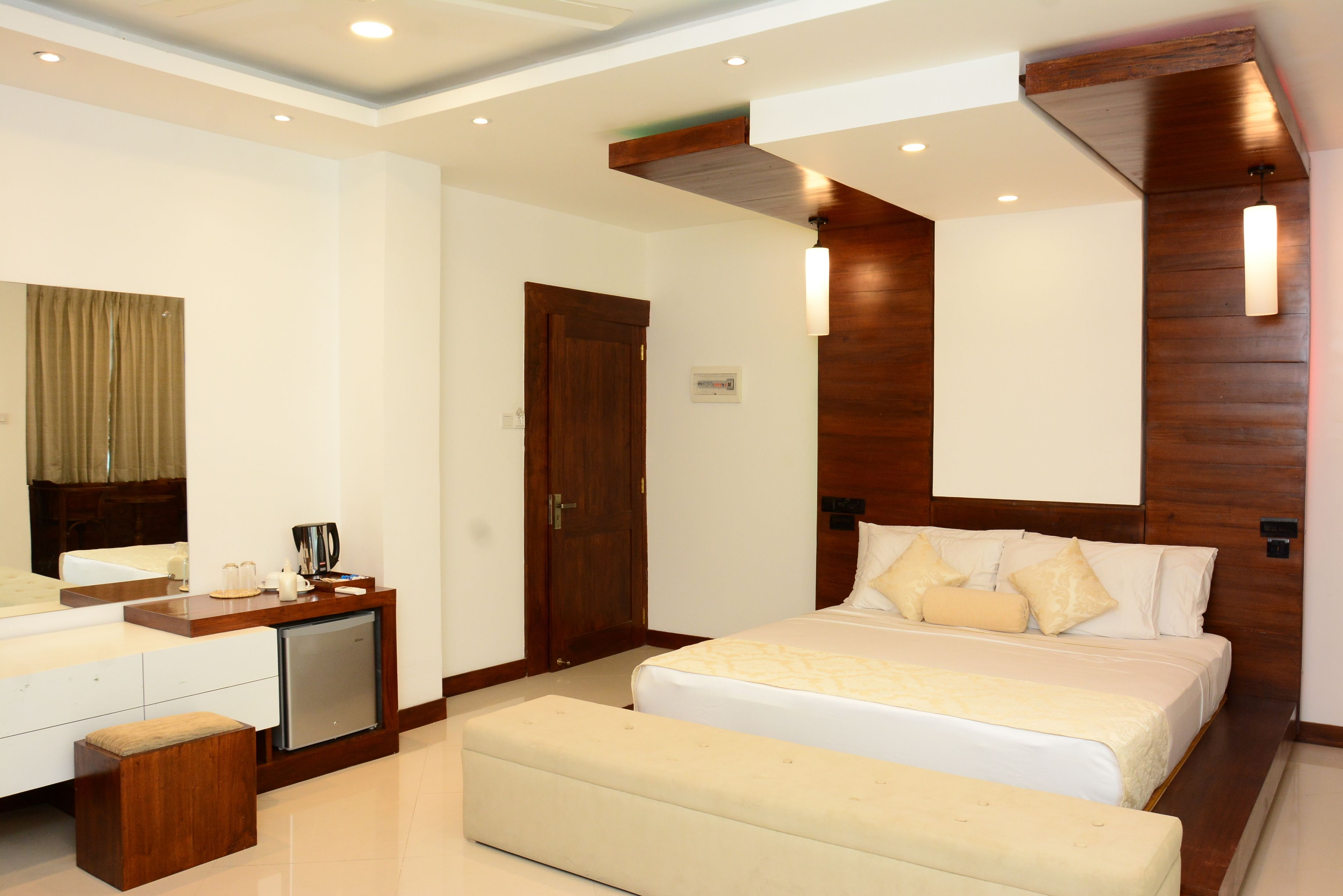 A hotel room with a bed, a desk, a small refrigerator, and a wooden accent wall.