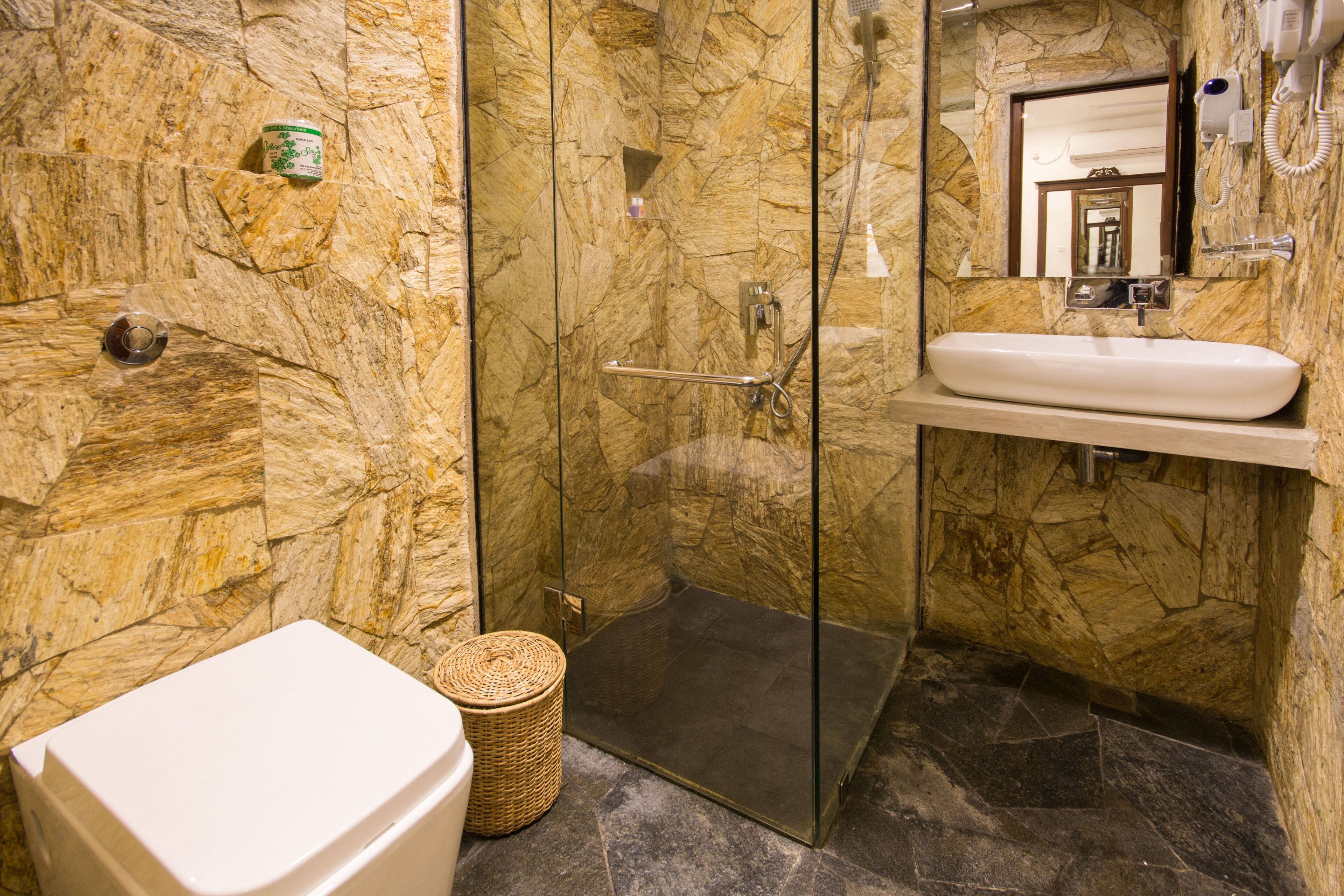 A bathroom with a stone wall, a glass shower enclosure, a white sink, and a toilet.