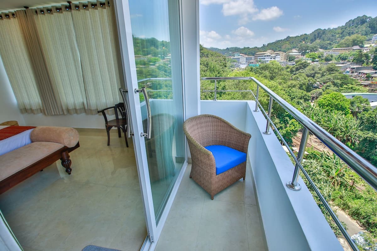 A balcony with a wicker chair and a sofa, a glass door, and a view of a green landscape.