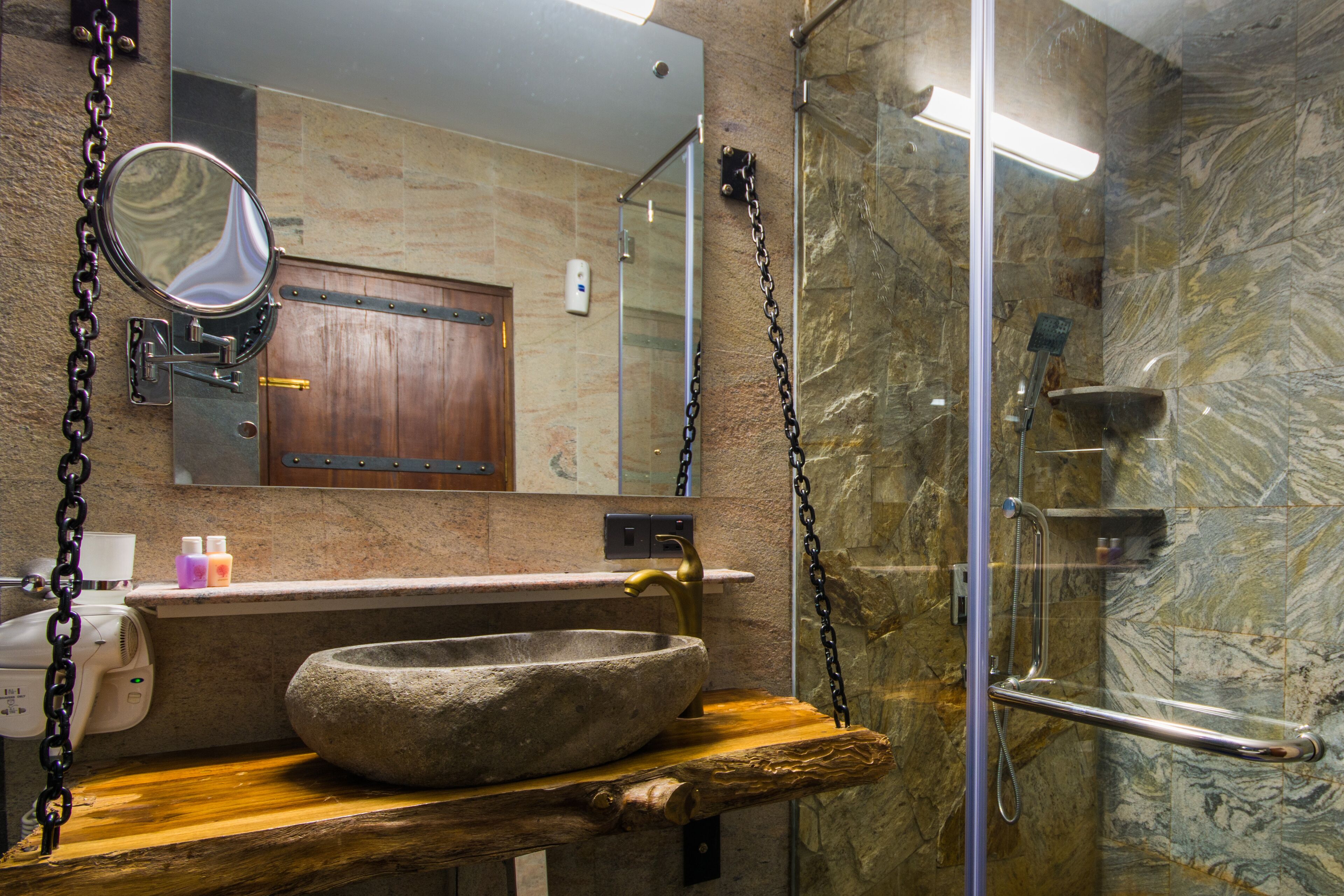 A bathroom with a stone sink, wooden shelf, and a glass shower enclosure.