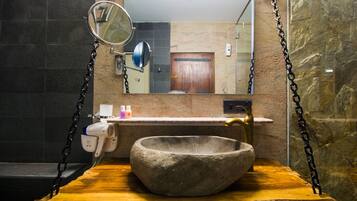 Un baño con lavamanos de piedra, un espejo y zona de ducha.