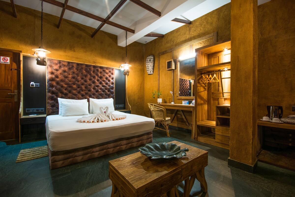 A hotel room with a large bed, a desk, a chair, and a small table with a decorative bowl.