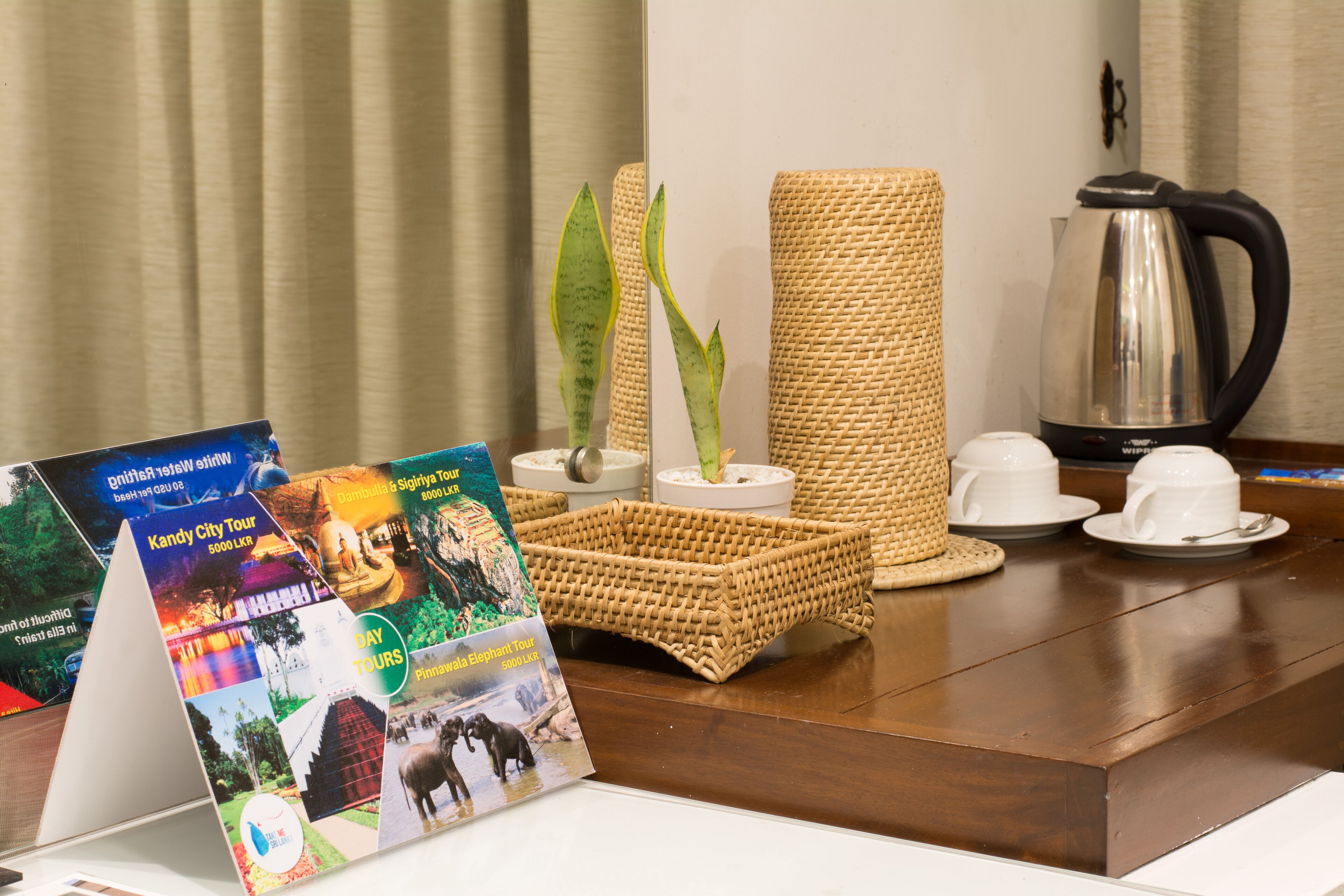 Un espace d’accueil d’hôtel avec un comptoir en bois, des brochures sur les circuits touristiques, un panier en osier, une plante en pot et une cafetière.
