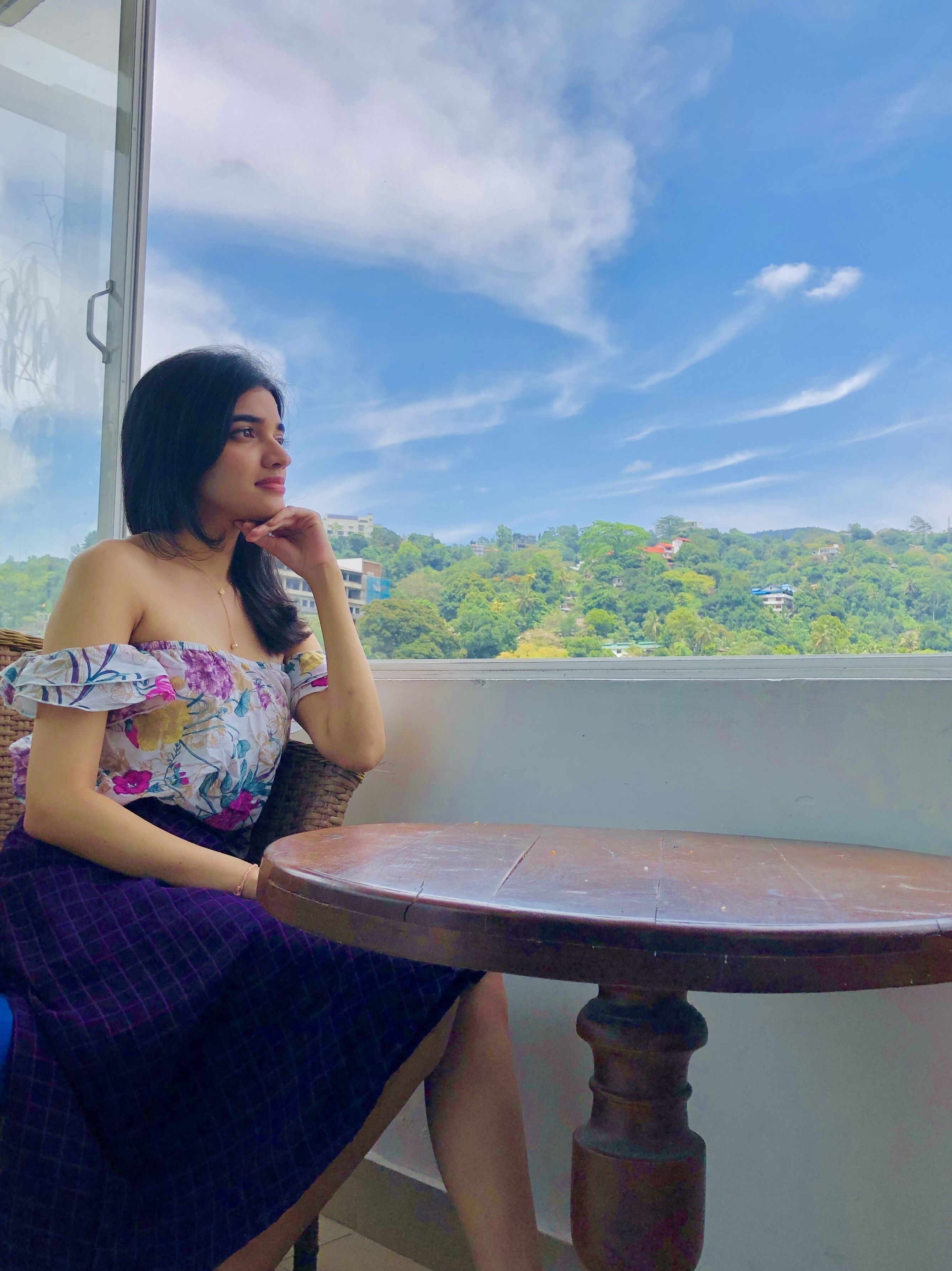 A person sitting on a balcony with a view of a green landscape and buildings.