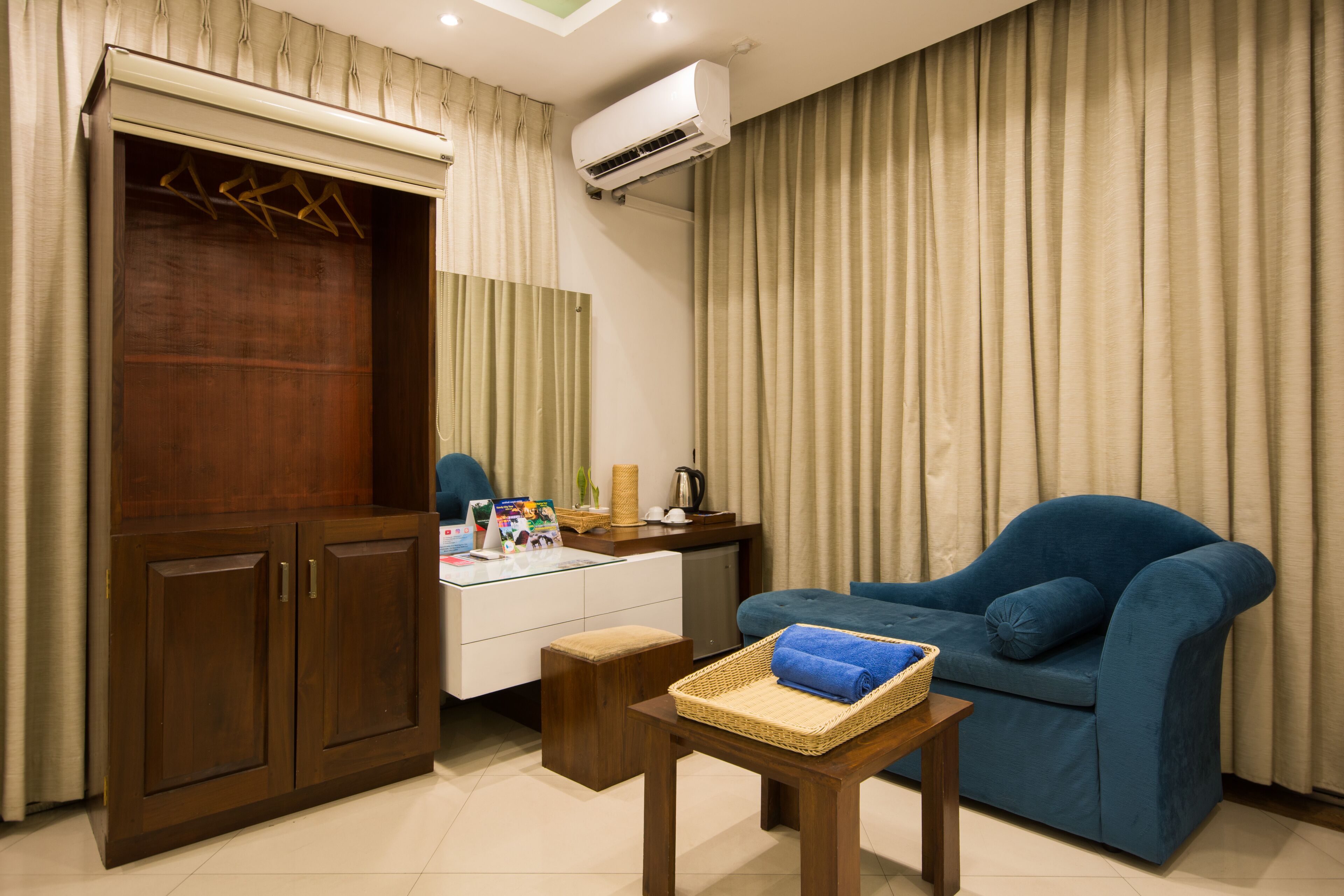 A room with a wooden wardrobe, a blue sofa, a small wooden table with a basket, and a desk with a chair.