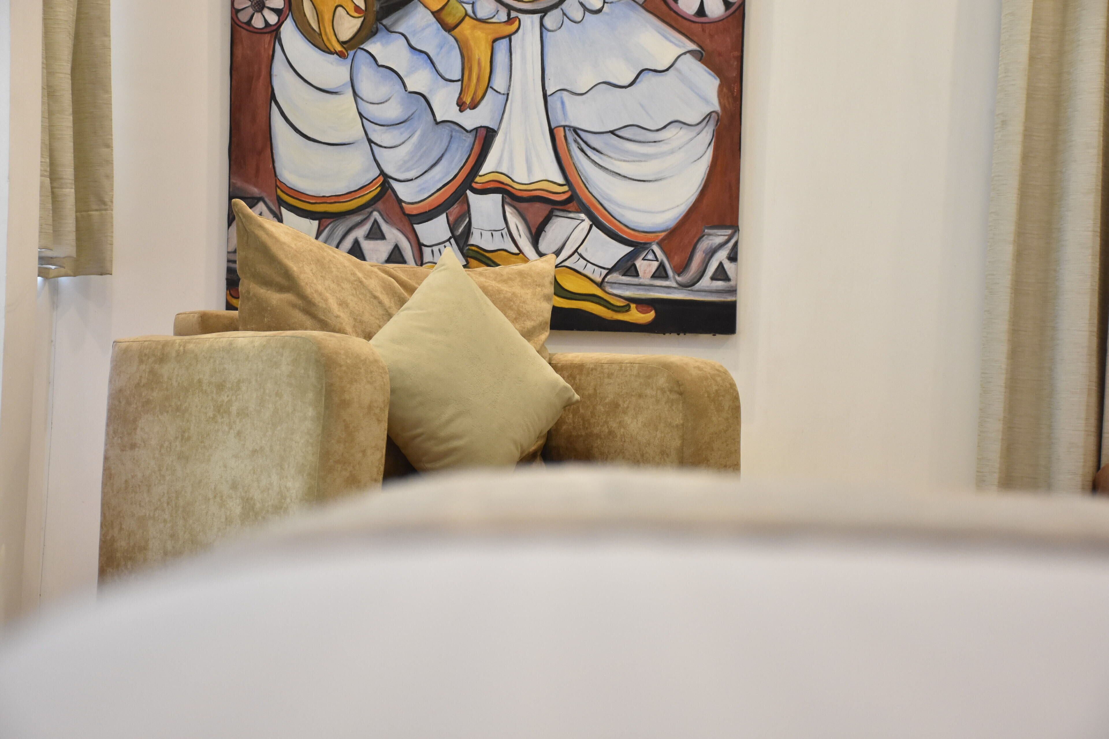 A room with a beige sofa, a large abstract painting, and a window with curtains.