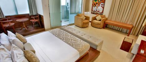 A hotel room with a large bed, two armchairs, a bench, a small table, and a painting on the wall.