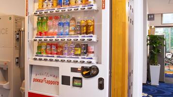 A vending machine with various drinks and snacks, located in a hotel lobby with a blue carpet and wooden accents.