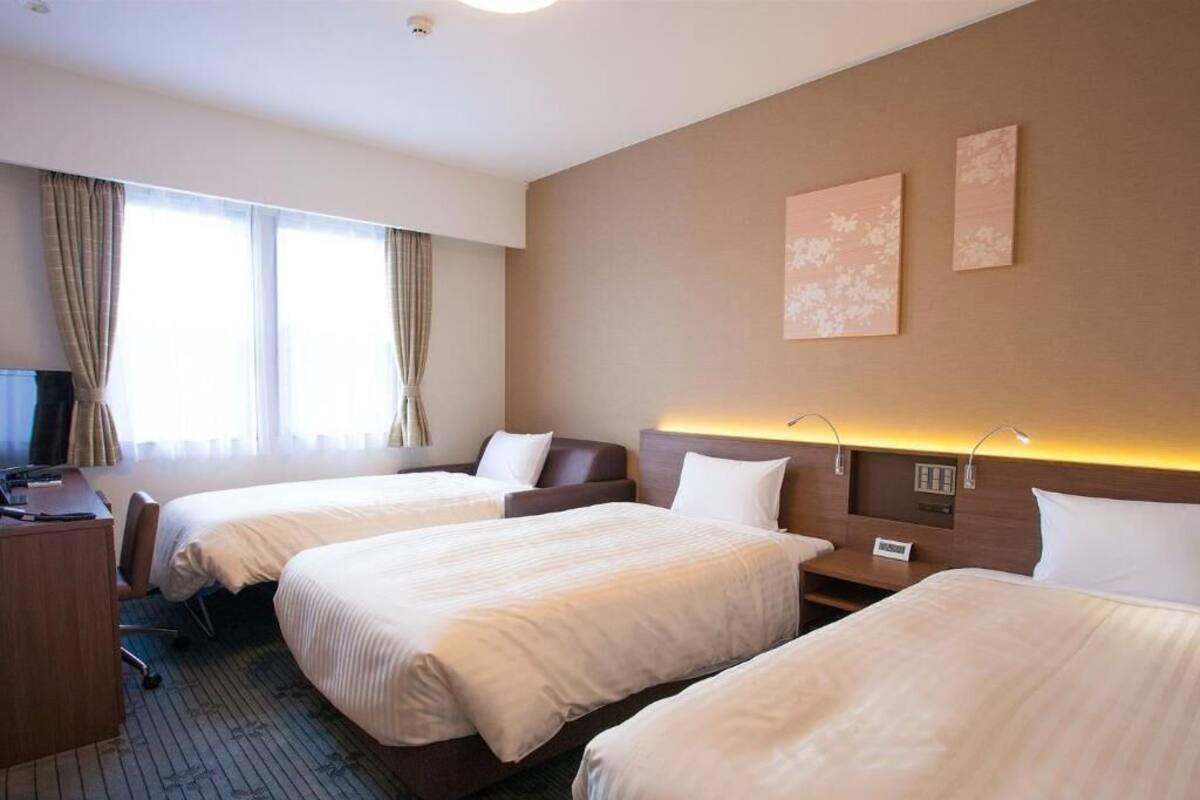 A hotel room with three beds, a desk, a chair, and a television.