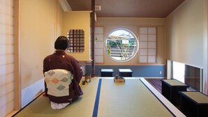 A traditional tatami mat room with a person seated facing a shoji screen.