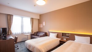 A hotel room with two beds, a desk, a chair, a small table, and a TV.