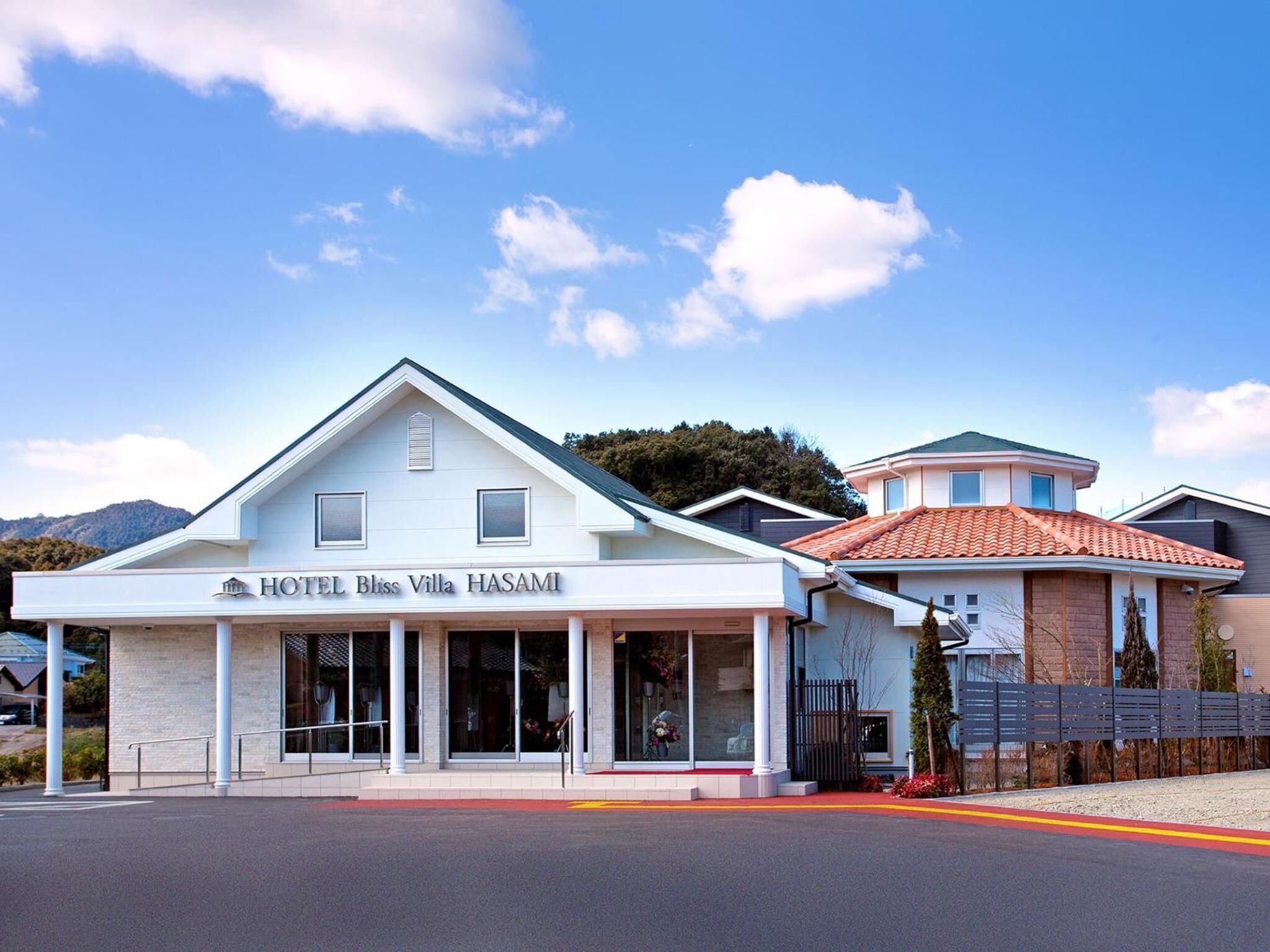 A two-story hotel with a white facade and a sign reading "HOTEL Bliss Villa HASAMI".