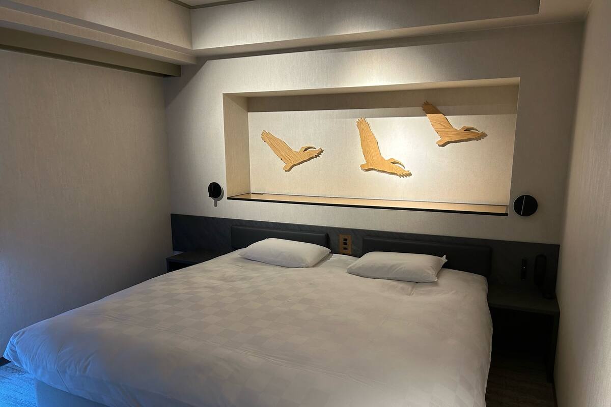 Hotelkamer met een groot bed, twee kussens, een hoofdbord met ingebouwde speakers en een wandlamp.
