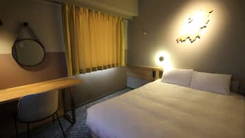 A hotel room with a bed, a desk, a chair, a window with curtains, a wall-mounted light, and a map decoration.