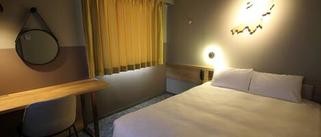 Una habitación de hotel con cama, escritorio, silla, ventana con cortinas, luz empotrada en la pared y un mapa decorativo.