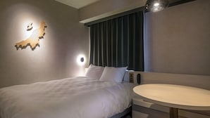 Une chambre d’hôtel moderne avec un lit soigneusement fait, une table ronde en bois et un luminaire fixé au mur.