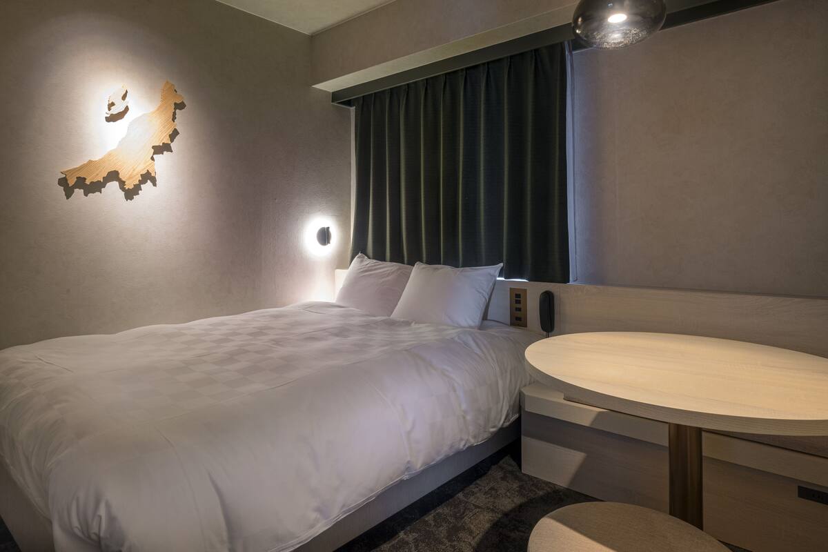 Een moderne hotelkamer met een net opgemaakt bed, een ronde houten tafel en een wandlamp.