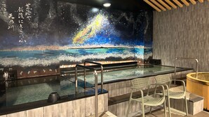 Un espace bien-être comprenant un grand mur décoré d’une fresque représentant un paysage marin, un jacuzzi en verre et un sauna en bois.