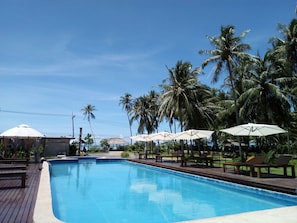 Una piscina con tumbonas y sombrillas, rodeada de palmeras.