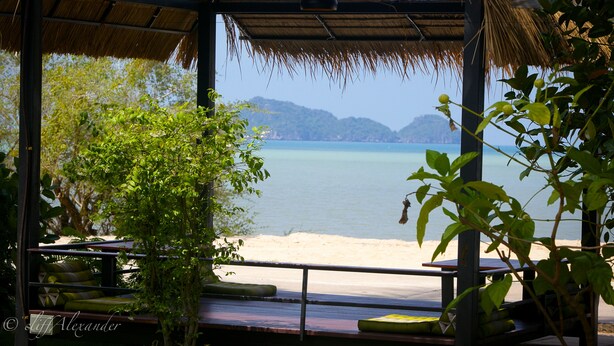 A beachside seating area with a thatched roof, overlooking a calm sea and distant hills. - The Ford Sunset Beach Resort (Ko Pha-ngan)