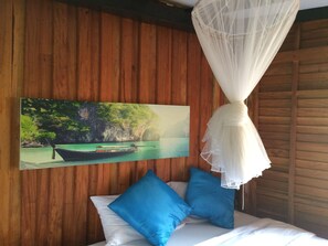 Un dormitorio con una cama, almohadas azules, un dosel blanco y un cuadro de un barco sobre el agua.
