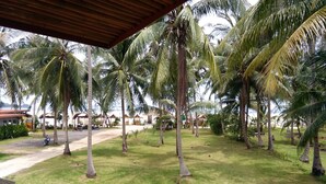 A tropical resort with palm trees, a covered seating area, and a road with parked vehicles. - The Ford Sunset Beach Resort (Ko Pha-ngan)