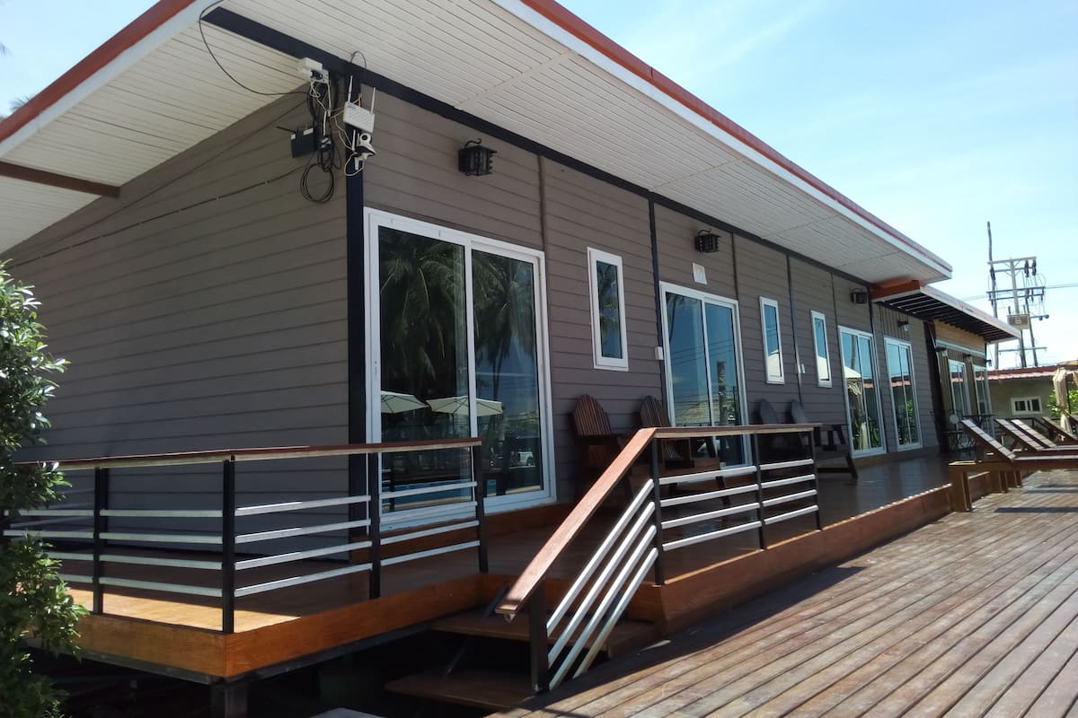 Een modern gebouw met een overdekt terras, grote ramen en een trap die naar de bovenverdieping leidt.