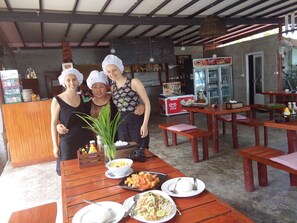 A restaurant with wooden tables and benches, a chalkboard menu, and a variety of dishes on the tables. - The Ford Sunset Beach Resort (Ko Pha-ngan)