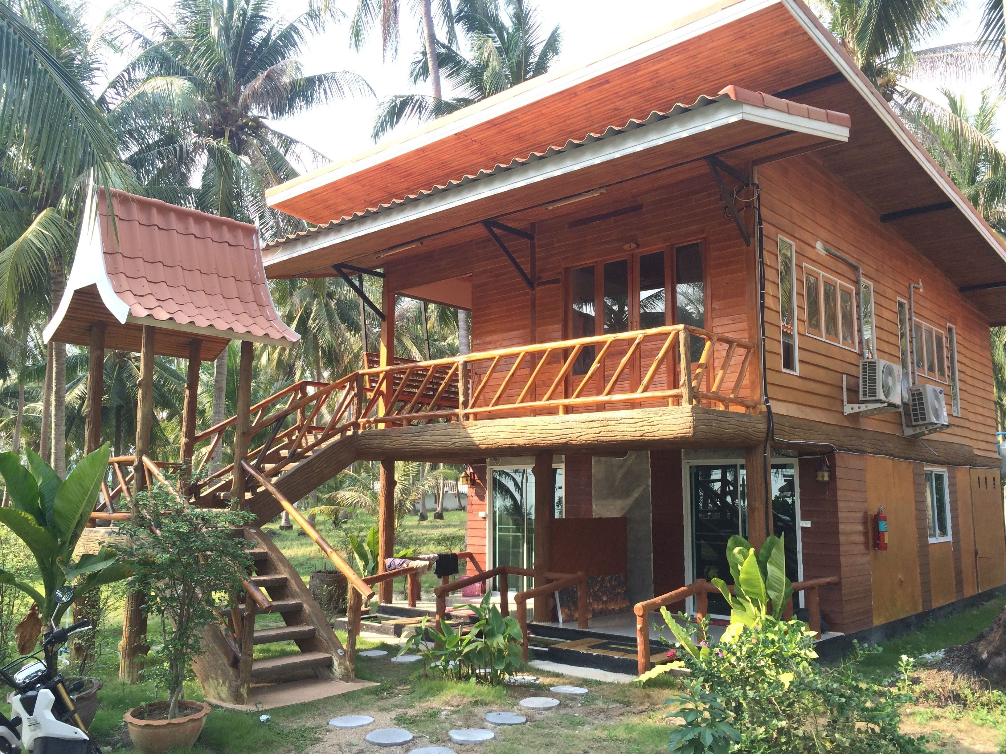 A wooden house with a balcony, a staircase, and a small garden area.