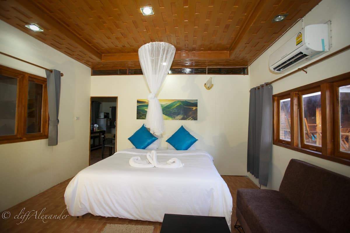 Een slaapkamer met een groot bed, een houten plafond en uitzicht op de omgeving door een raam.
