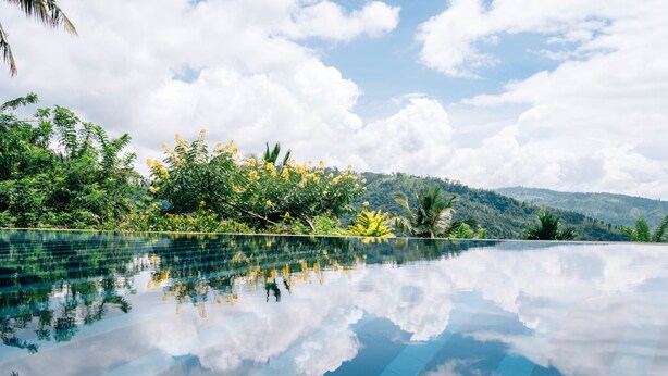 A clear view of an infinity pool reflecting the sky and surrounding greenery. - Mount Havana (Udapalatha)
