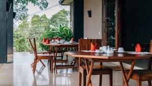 A dining area with wooden tables and chairs, a view of greenery outside, and a modern architectural design. - Mount Havana (Udapalatha)