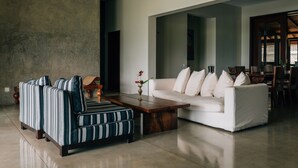 A modern living room with a sofa, striped armchairs, a coffee table, and a dining area in the background. - Mount Havana (Udapalatha)