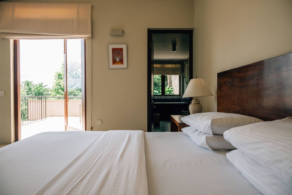 Habitación de hotel con una cama grande, una mesita de noche, una lámpara, un cuadro enmarcado y una puerta corrediza que da a un balcón.