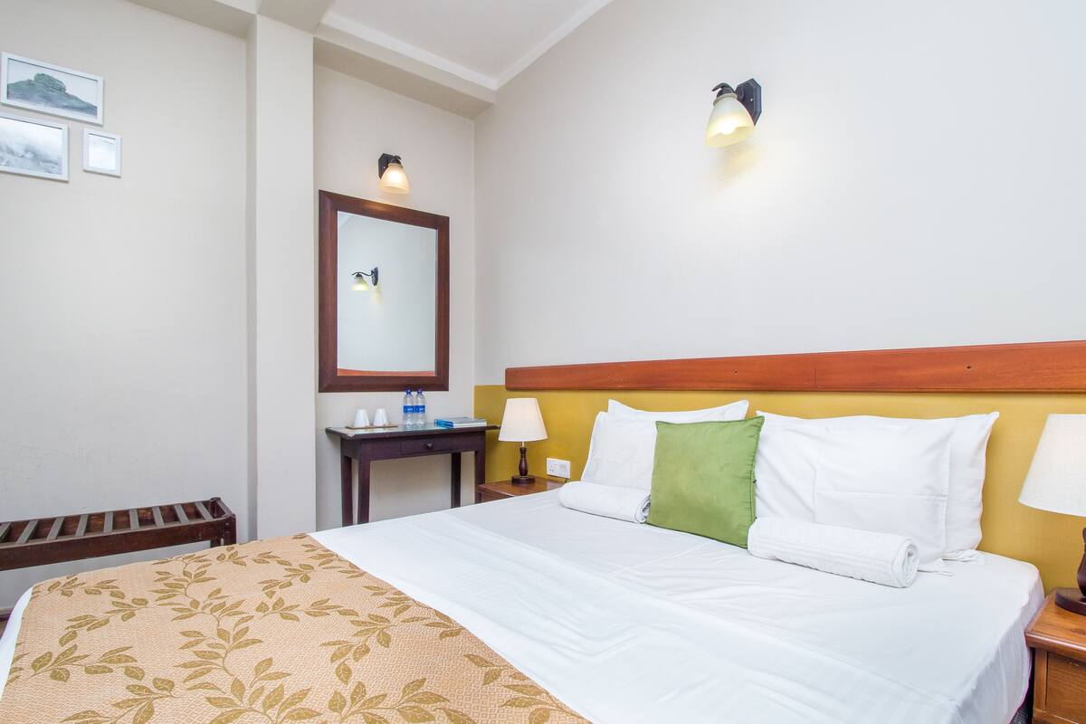 A hotel room with a bed, a desk, a chair, and a mirror.