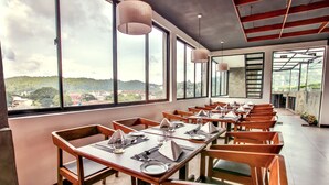 Ein Restaurant mit Holztischen und -stühlen, große Fenster mit Blick auf die Stadt.