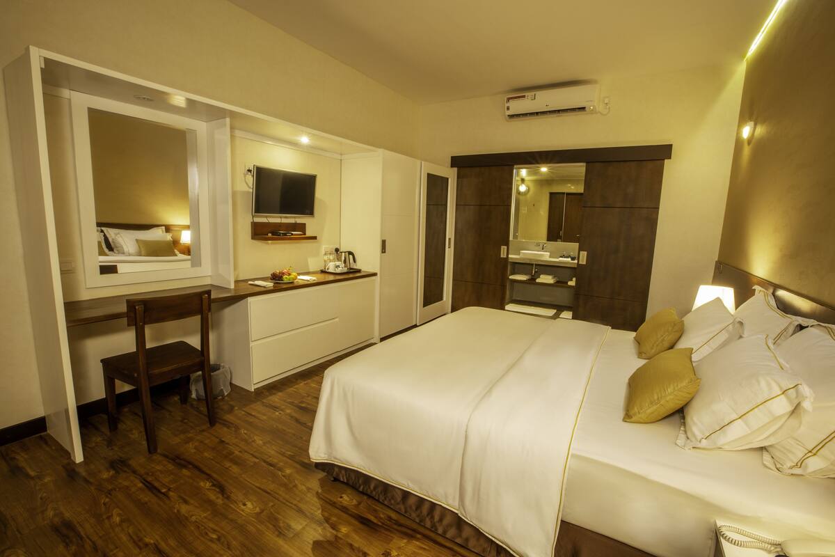 A hotel room with a bed, a desk, a chair, a television, a mirror, and a bathroom.