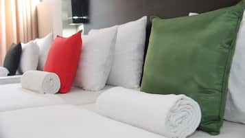 Una cama bien hecha con almohadas blancas y verdes, una toalla blanca enrollada y un cojín rojo.