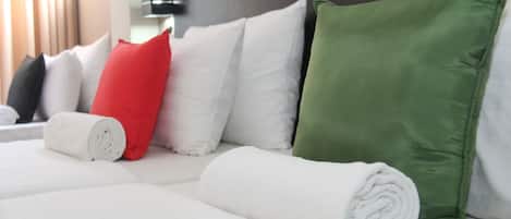 A neatly made bed with white and green pillows, a rolled white towel, and a red pillow.