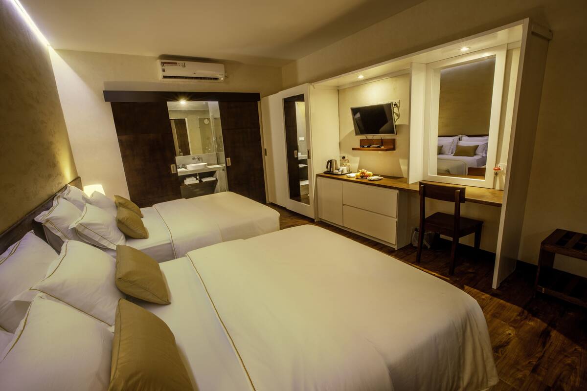 A hotel room with two beds, a desk, a TV, and a mirror.