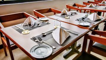 Un comedor con mesas dispuestas para cuatro, cada una con un sitio que incluye platos, cubiertos y servilletas.