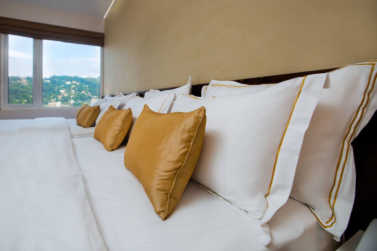 A hotel room with a large bed, white linens, and gold accents.