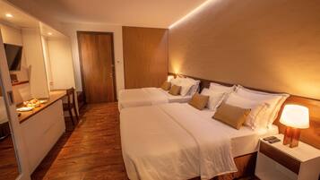Une chambre d’hôtel avec deux lits, un plancher en bois, un bureau avec une chaise et un téléviseur fixé au mur.