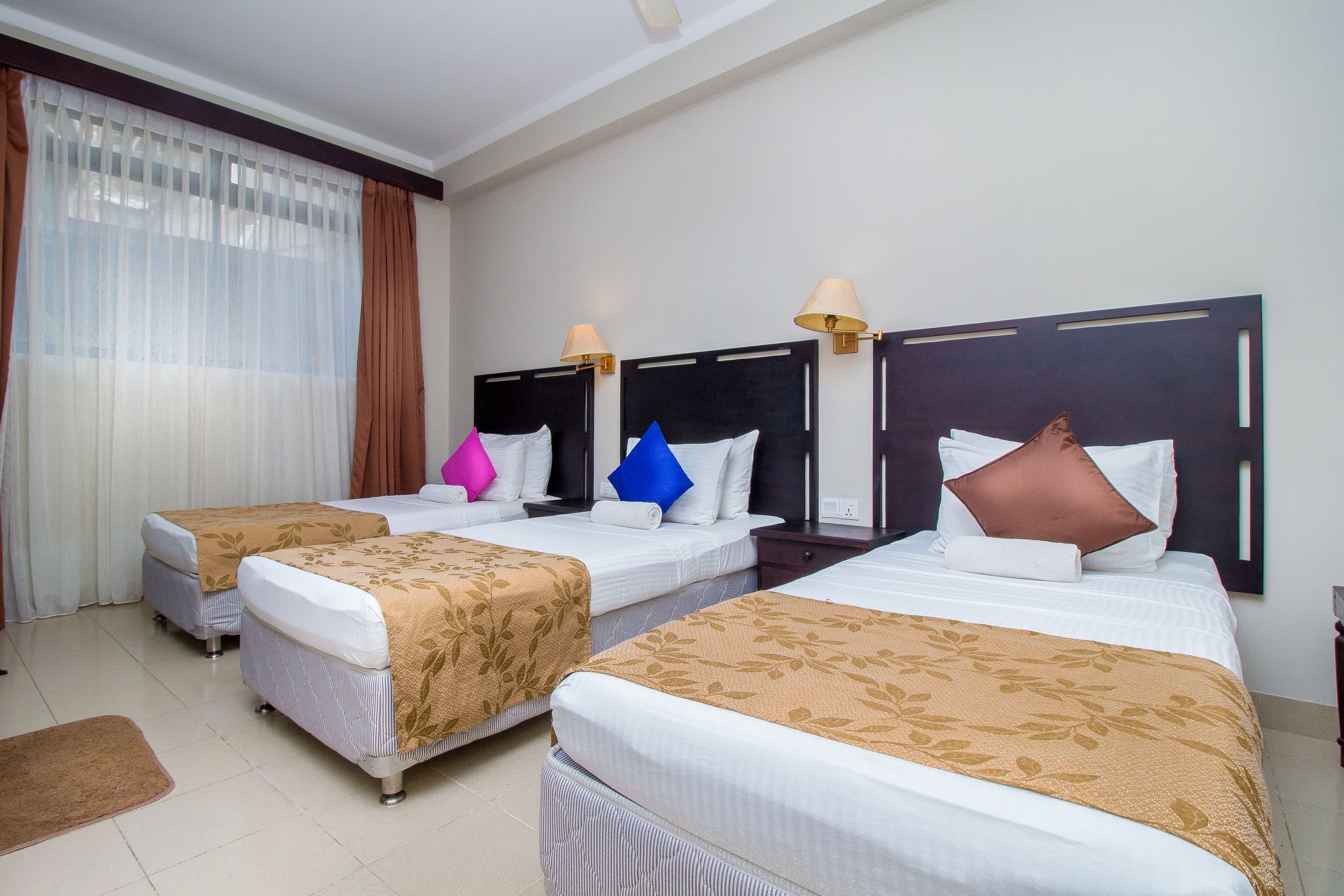 A hotel room with three beds, each with a headboard and bedside lamps.